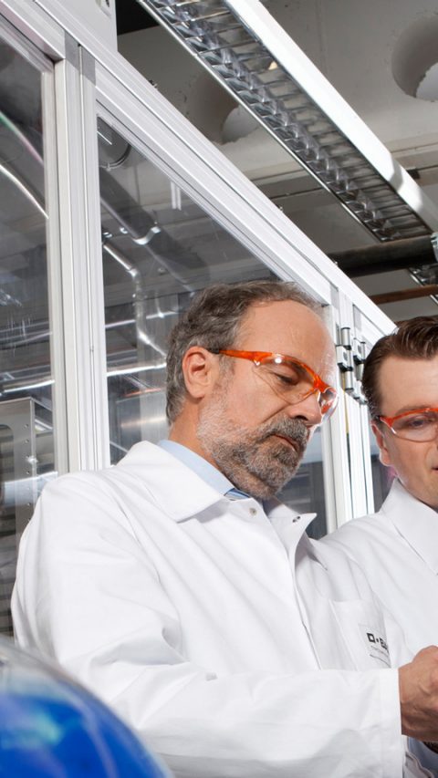 Two scientist wear red safety goggles analyzing chemical holding cue cards 