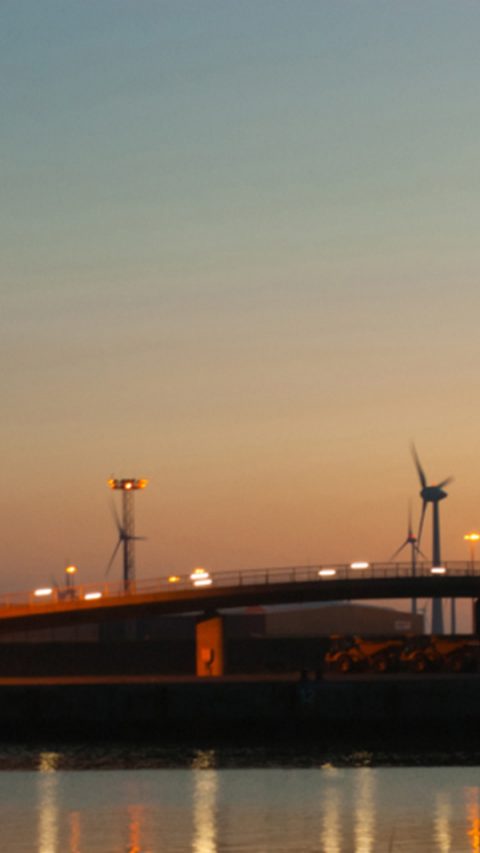 Landscape view of a bridge by the water with windmills during sunset 