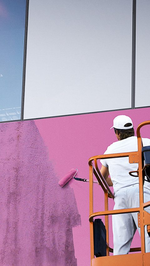 Painter on an industrial lift painting a building pink