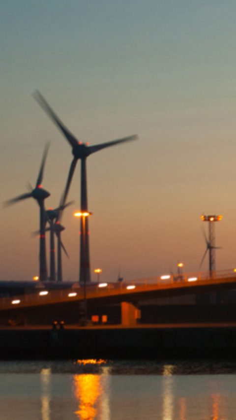 Landscape view of a bridge by the water with windmills during sunset 